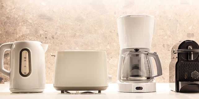 An electric tea kettle, toaster, coffee machine, and espresso machine sit in a row