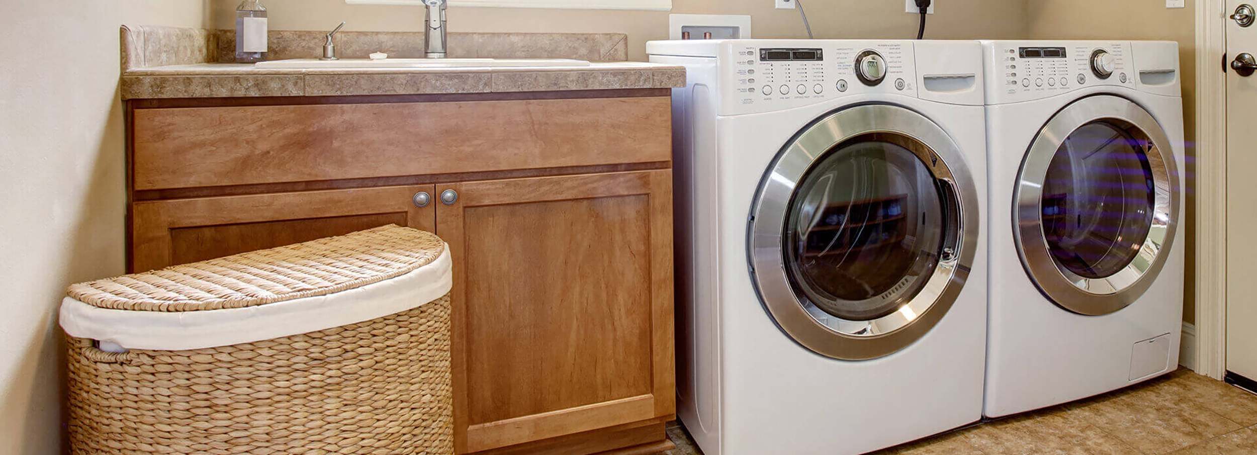 : White washing machine and dryer beside sink in tidy home laundry room.