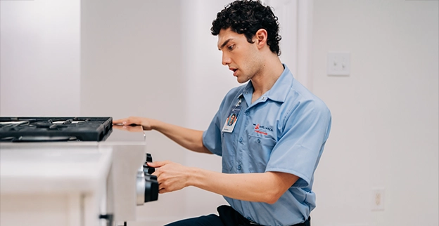 A Mr. Appliance technician inspecting a kitchen range.