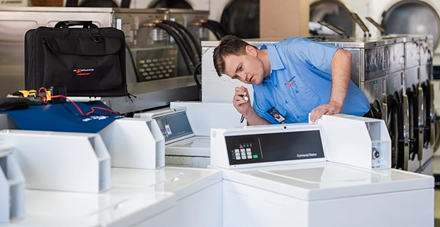 A Mr. Appliance technician inspects commercial washing machine units.