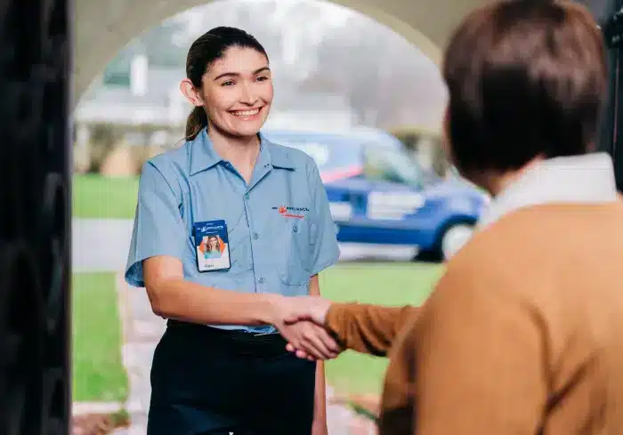Smiling service professional shaking hands with a customer outside a residential home with a service van in the background.