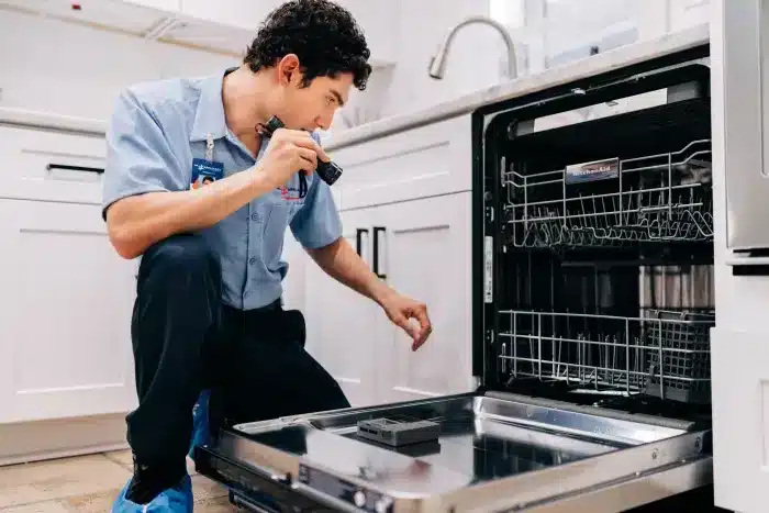 Mr. Appliance service professional using a flashlight to inspect inside an open dishwasher.