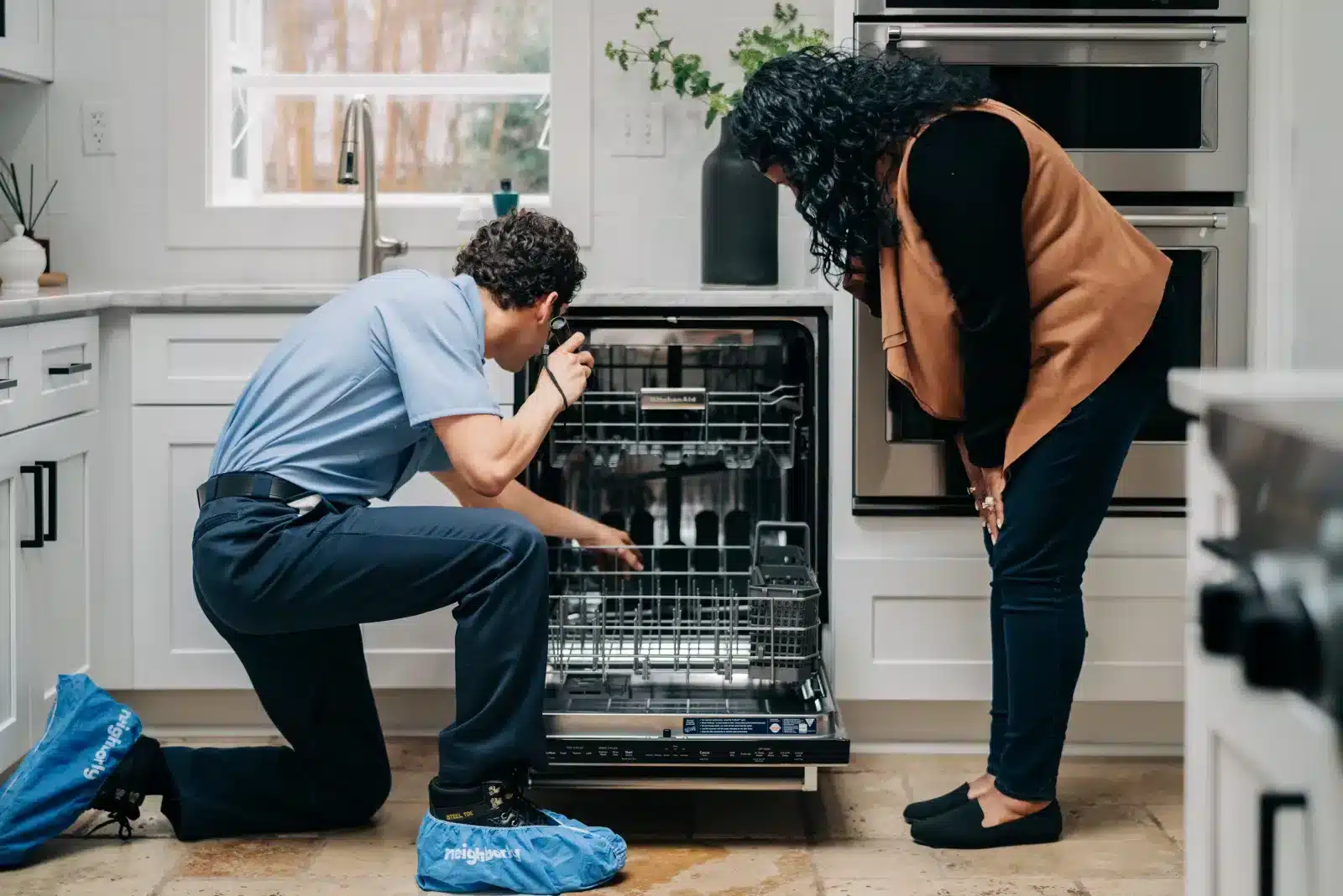 Mr. Appliance service professional inspecting an open dishwasher with a flashlight alongside a homeowner.
