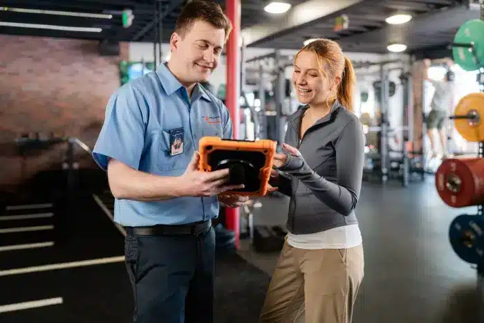 Mr. Appliance service professional showing a digital tablet estimate to a customer inside a fitness gym.