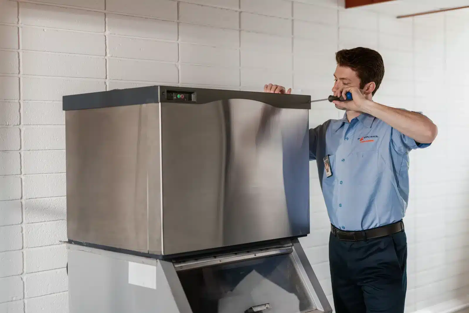 Appliance repair professional performing maintenance on a large stainless steel ice machine.