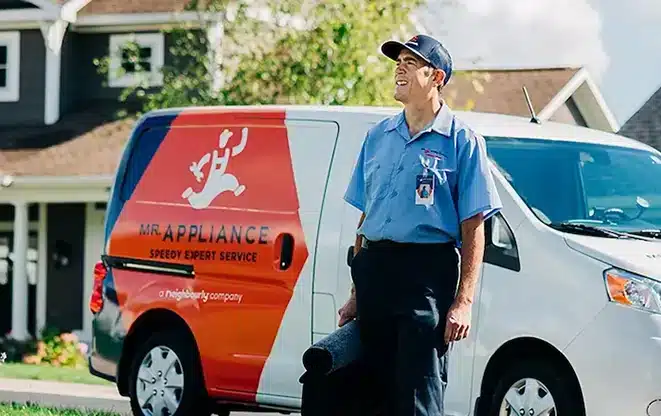 Uniformed Mr. Appliance service professional standing outside a residential home next to a company service van.