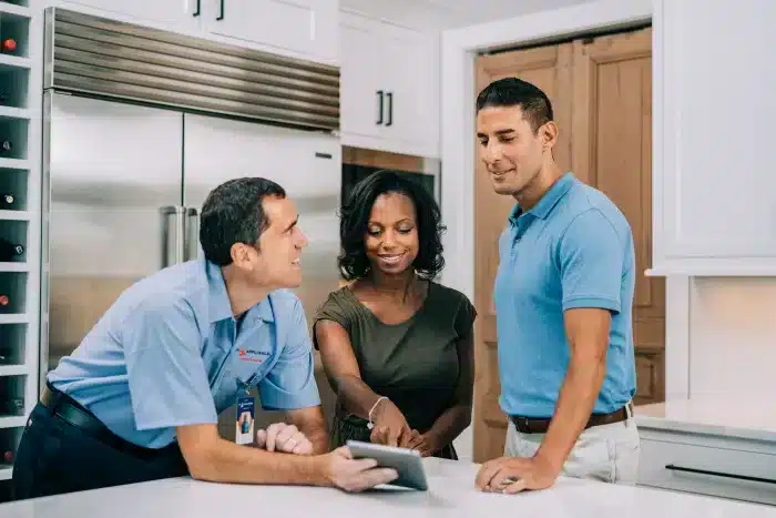 Mr. Appliance service professional showing a digital tablet to a couple in a modern kitchen.