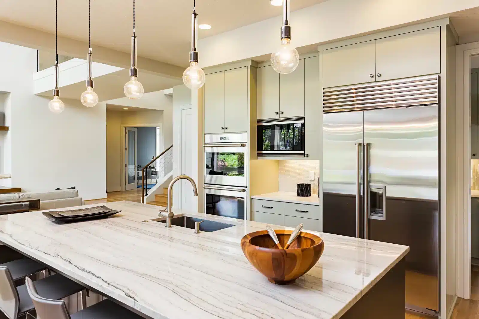 Modern kitchen featuring a built-in stainless steel refrigerator, double wall ovens, and a marble island.