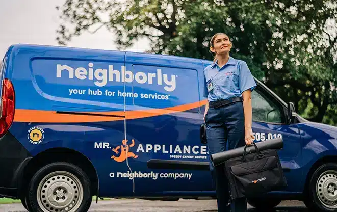 Uniformed appliance service professional carrying equipment outside next to a service van.