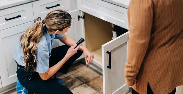 Mr. Appliance service professional shining flashlight underneath sink.
