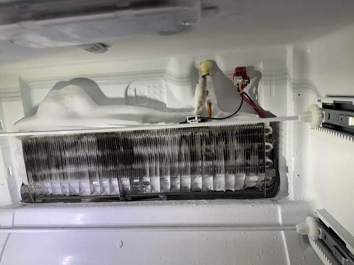 An evaporator coil of a refrigerator with too much frost on top.
