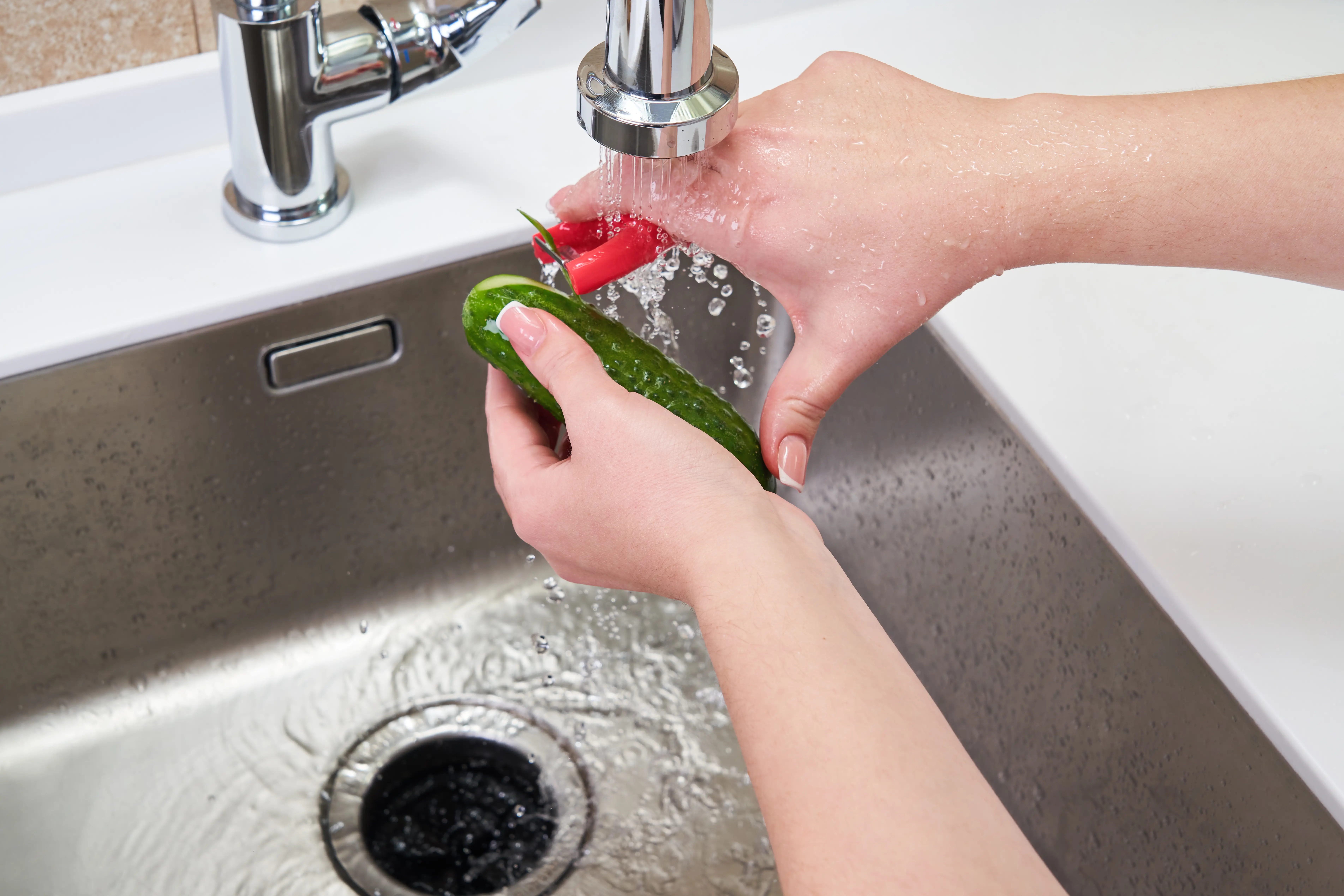 woman peeling a cucumber over a sink with a garbage disposal