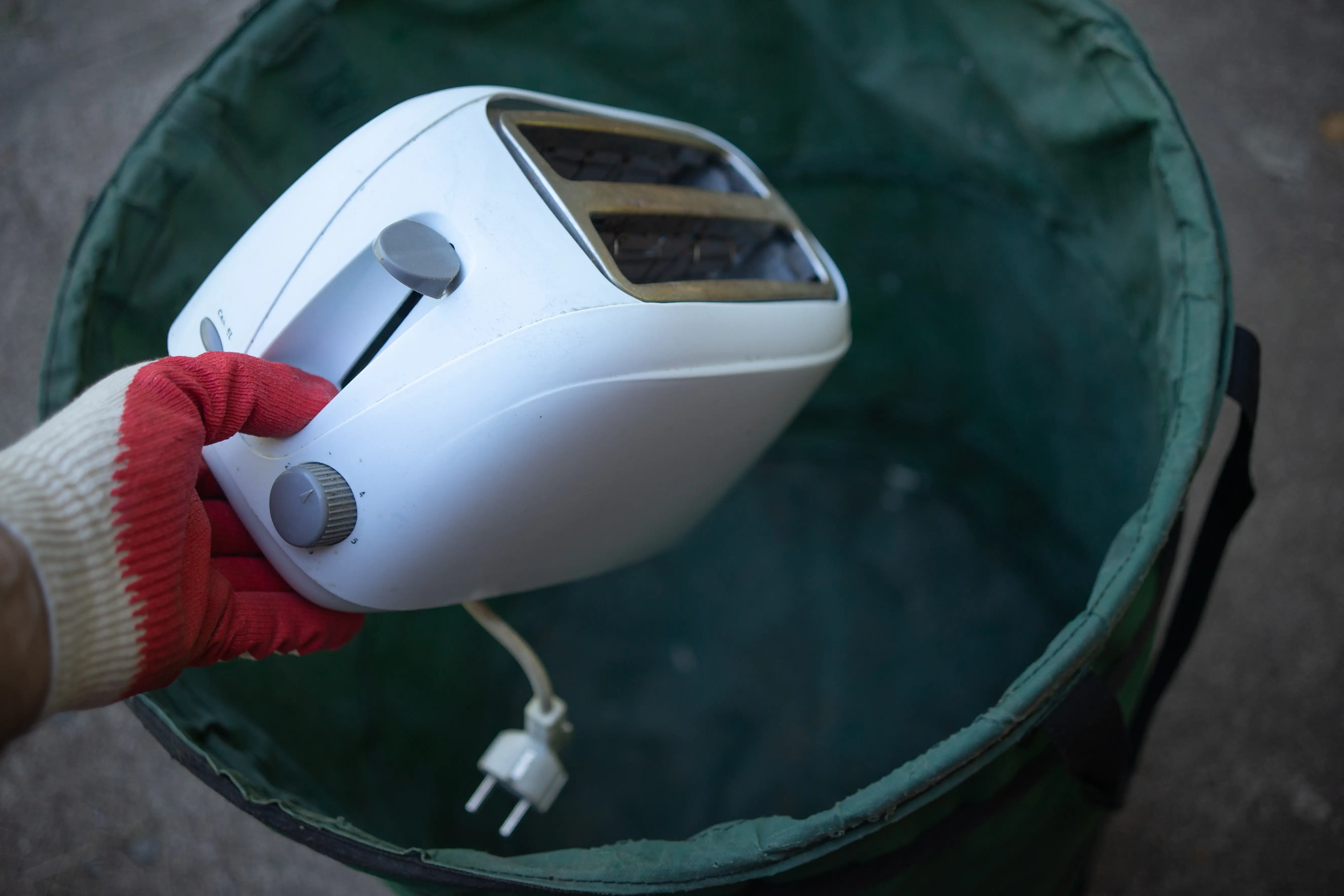 Hand throwing toaster into recycling bin