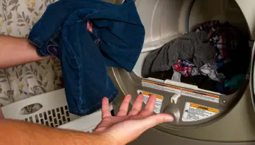 Man grabbing wet clothes out of a dryer.