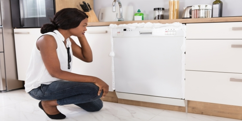 Woman kneeling in front of dishwasher with white foam coming from the machine.