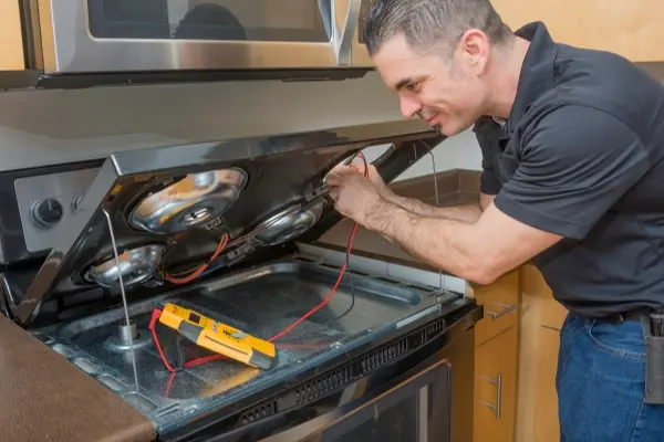 Professional electrician troubleshooting an electric stove top burner with a multi-meter. Taken inside of an apartment.