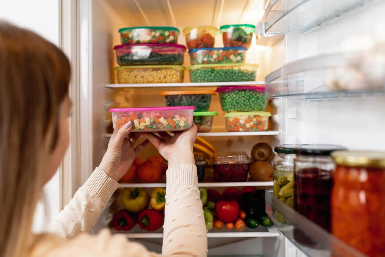 Woman placing food in an open refrigerator