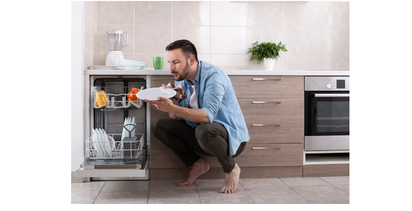 Man inspecting a plate over open dishwasher