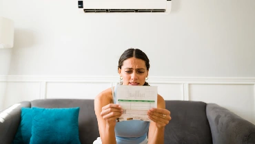 Woman sitting on a sofa and holding a paper electric bill in both hands, furrowing her brow in confusion
