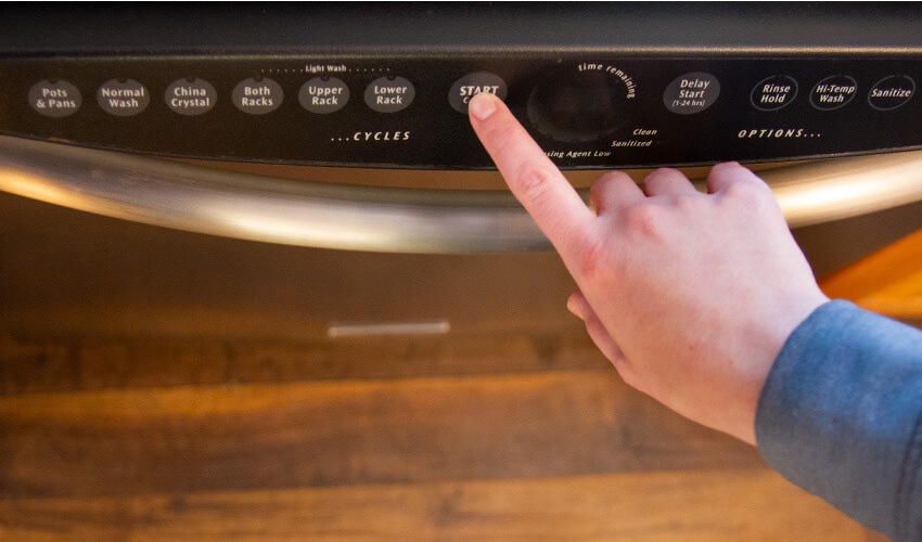 Person pressing start button on dishwasher