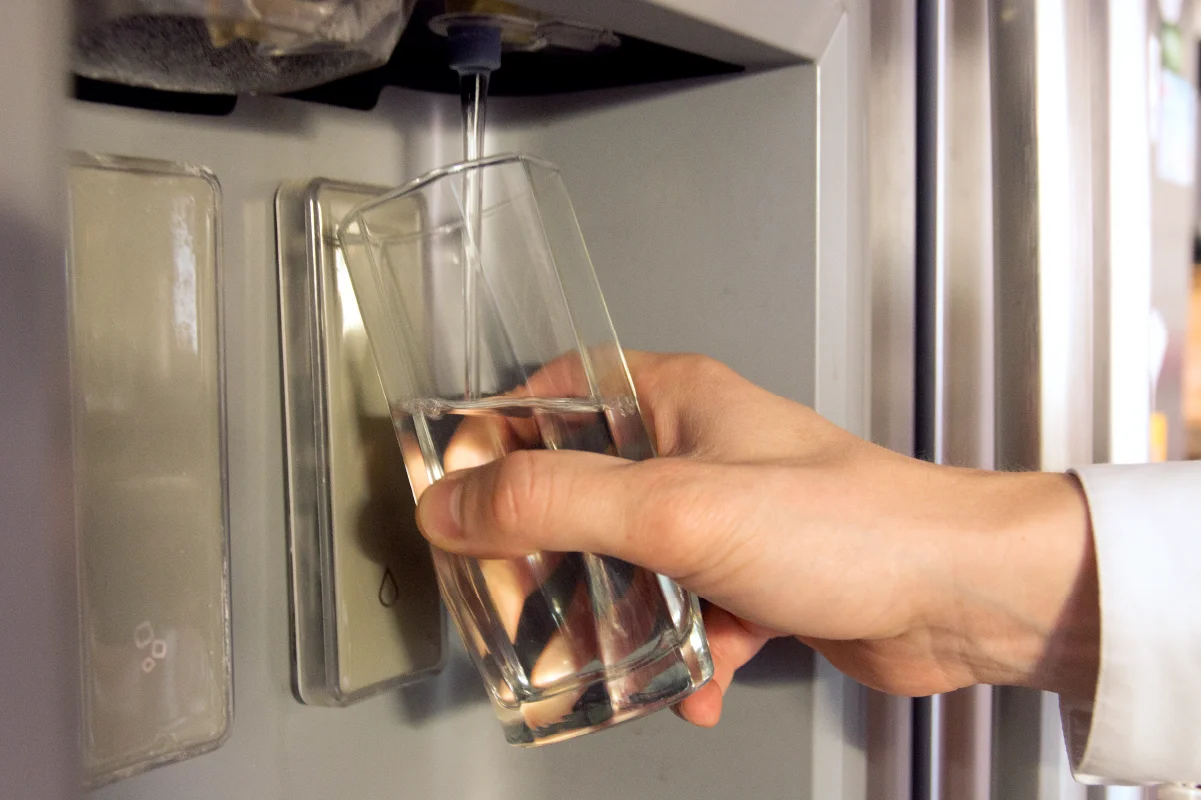 Person filling a clear glass with water from a refrigerator water dispenser