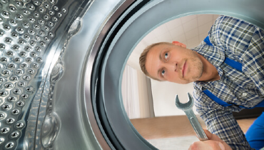 Man holding a wrench and looking into the basin of a washing machine.