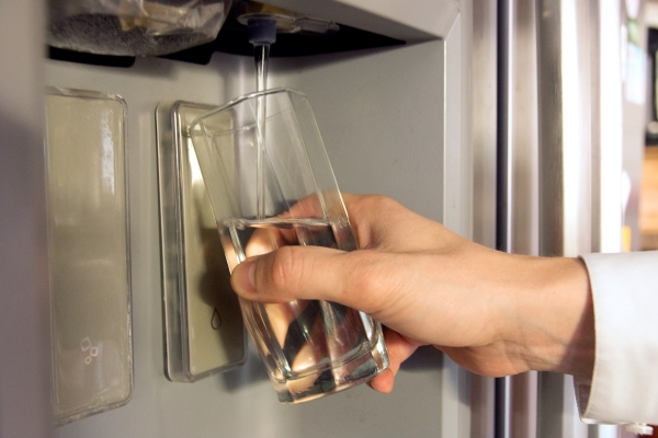 Man holding glass up to refrigerator and filling with water from dispenser