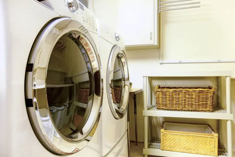 Washer and dryer in a utility room, next to a shelf holding two large wicker baskets.