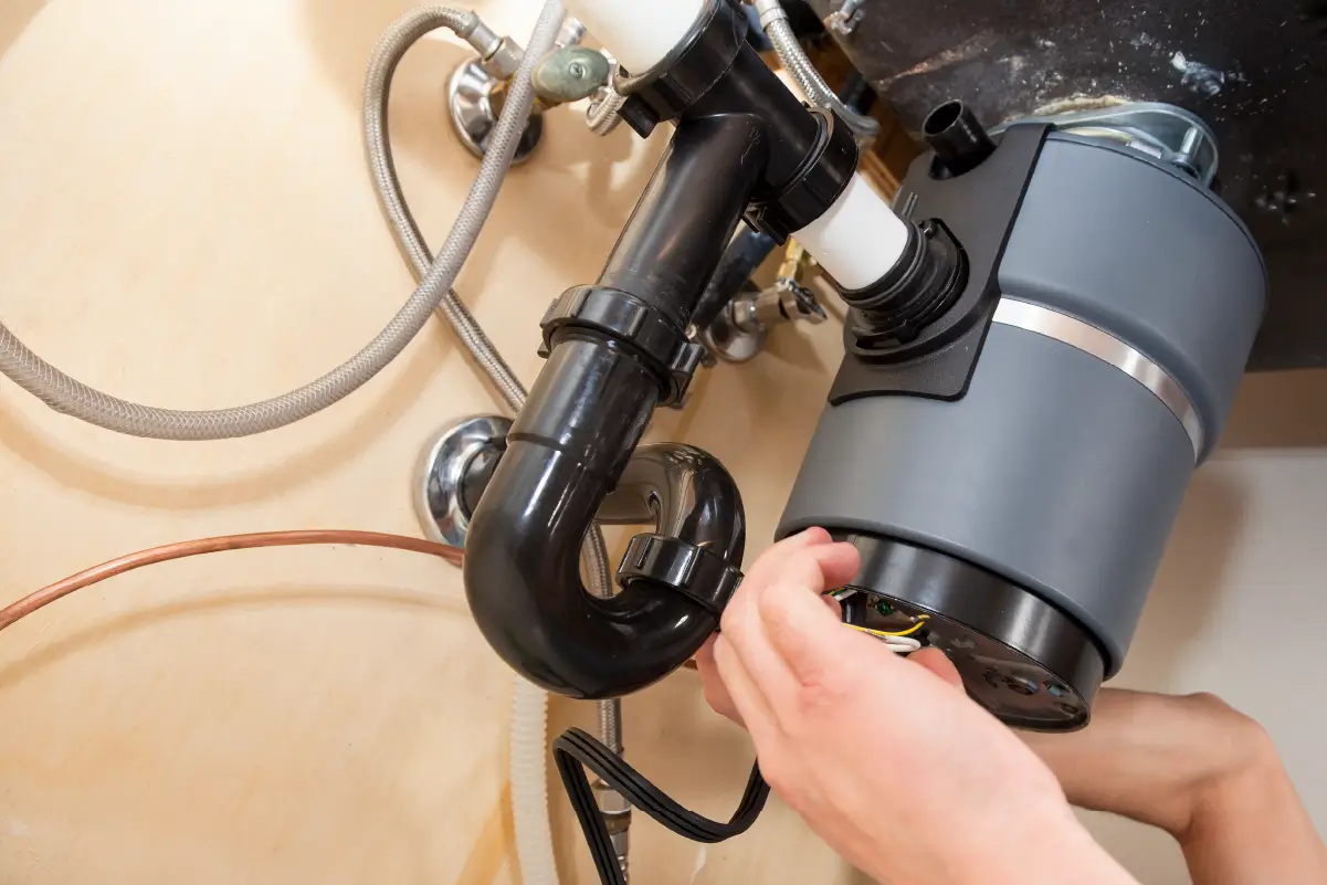 A person checking the fittings of a garburator under their sink.