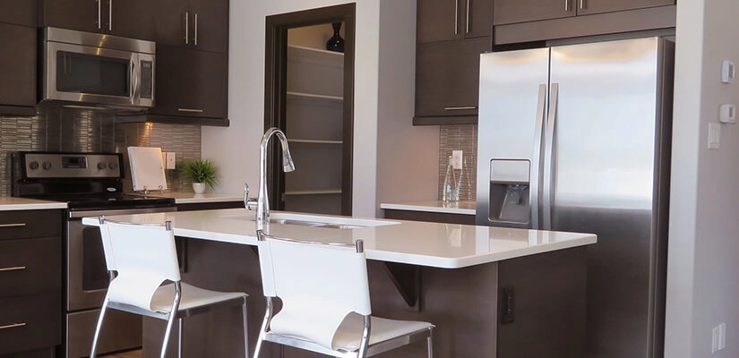 Kitchen with appliances including a refrigerator behind an island with an embedded sink