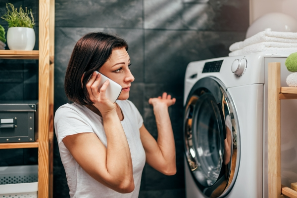 Woman on cell phone sitting in a laundry room calling for appliance repair
