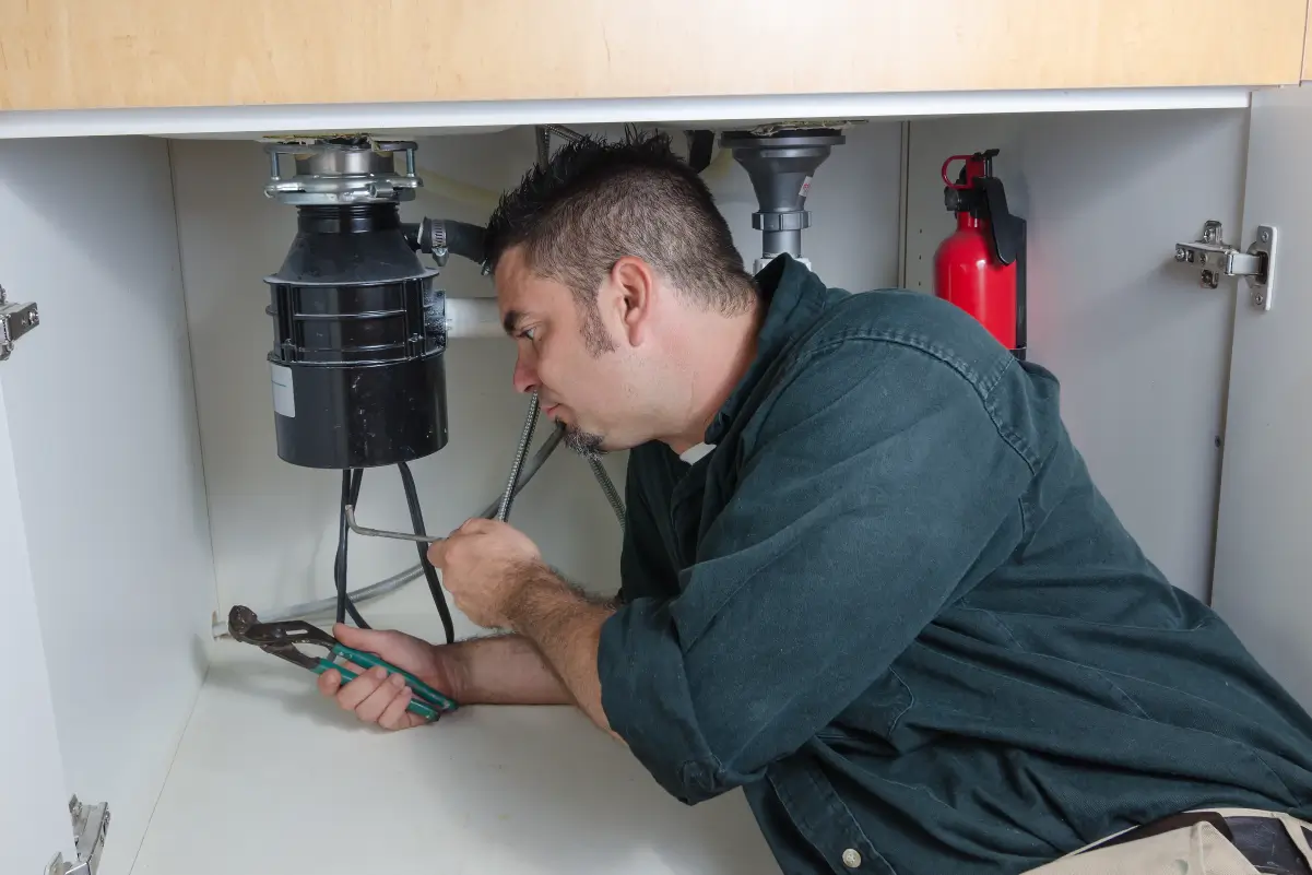 A homeowner underneath a sink unclogging a garbage disposal.