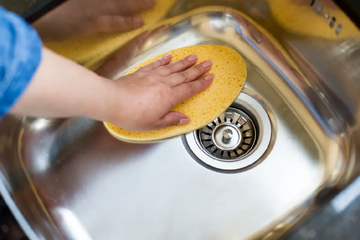 person wiping down stainless steel sink with yellow sponge