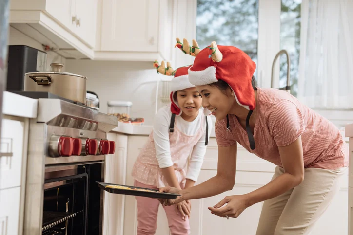 Mom and daughter putting holiday cookies in the oven 