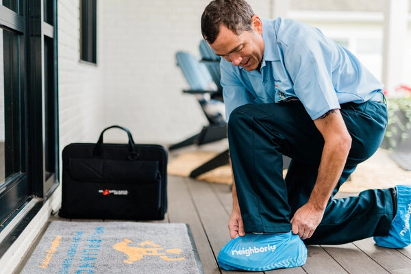 Mr. Appliance service professional at homeowner's residence with doormat, tool, and shoe covers 