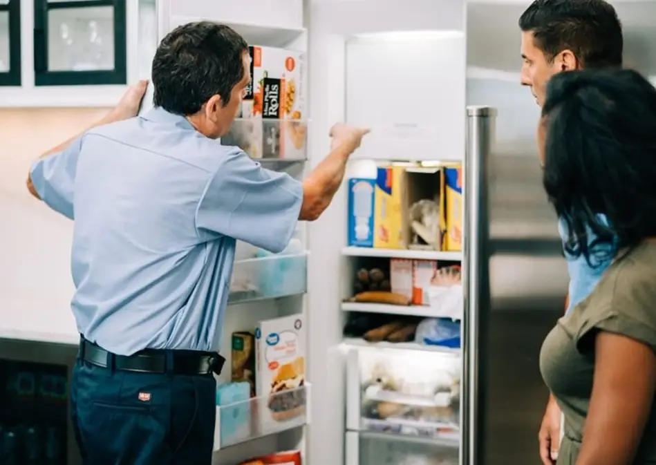 Mr. Appliance tech pointing into freezer and discussing repairs with homeowners.