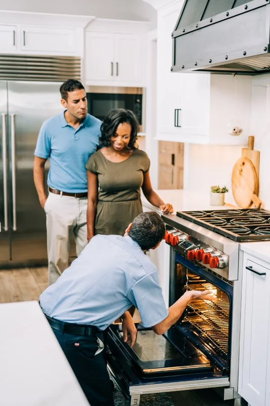 Mr. Appliance repairman inspecting an oven in front of customers.