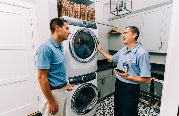 Mr. Appliance service professional assessing washing machine and dryer with homeowner