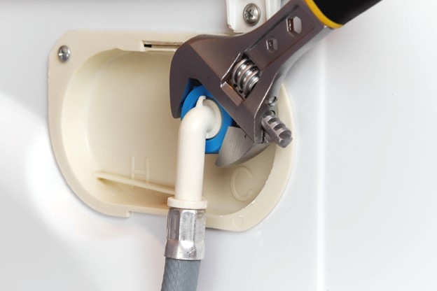 A wrench working on connecting a water supply hose to a washing machine.