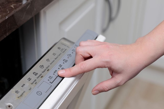 Woman’s hand pressing button on dishwasher touchpad.