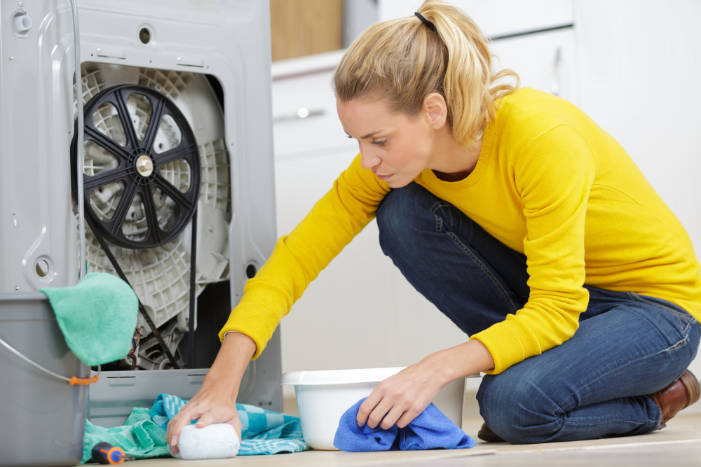 Woman sitting on the floor cleaning a water from leaking washing machine.