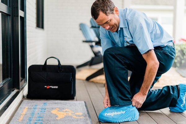 Mr. Appliance service professional at homeowner's residence with doormat, tool, and shoe covers