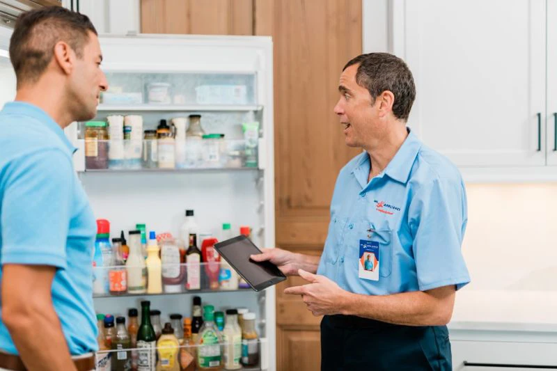 Mr. Appliance tech explaining Bosch appliance repair services to customer in front of an open fridge