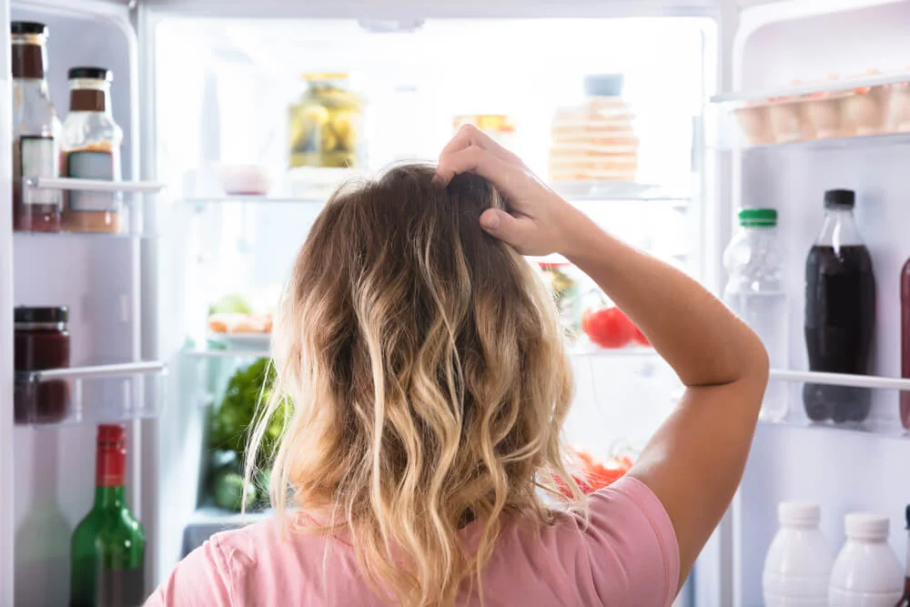 woman scratching head while looking at fridge