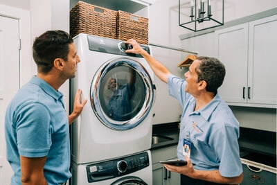 A Mr. Appliance technician adjusting a dryer knob while his customer watches