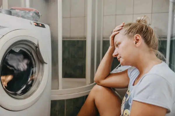 Woman sitting in front of a broken front-load washing machine.