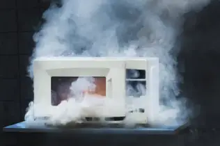 Front view of a white microwave oven with smoke surrounding it.