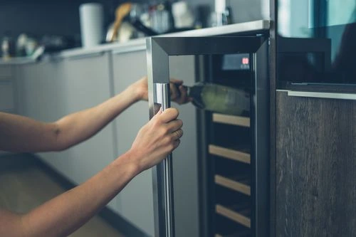 Woman’s hands pulling wine out of a wine cooler.